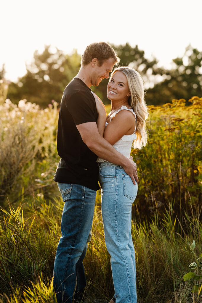 Engaged couple sharing a playful moment in a lush Bemidji field during golden hour