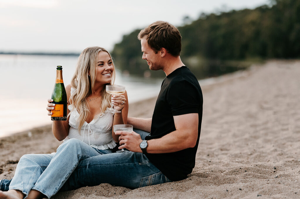 Engaged couple sharing a playful moment drinking champagne on the beach