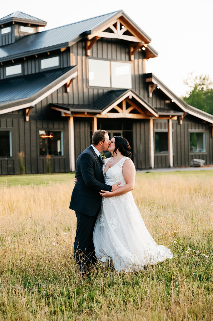 Newlyweds share a romantic embrace in a serene field, with the Ivy Black's natural beauty as the backdrop