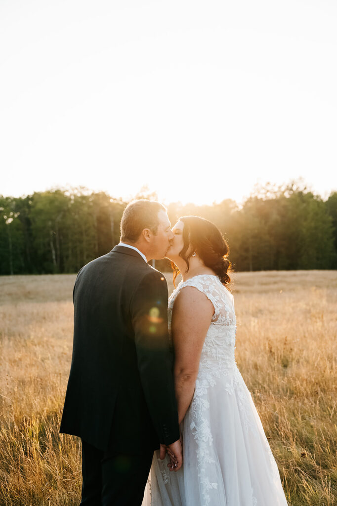 Newlyweds share a romantic embrace in a serene field, with the Ivy Black's natural beauty as the backdrop