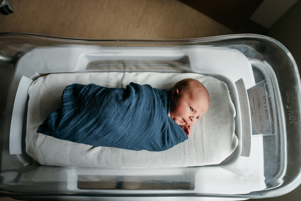 Newborn baby resting peacefully in a hospital bassinet with soft, natural light highlighting delicate features during a Fresh 48 photography session