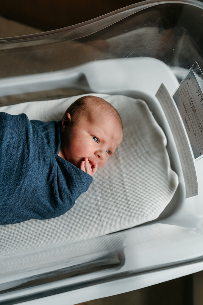 Newborn baby resting peacefully in a hospital bassinet with soft, natural light highlighting delicate features during a Fresh 48 photography session