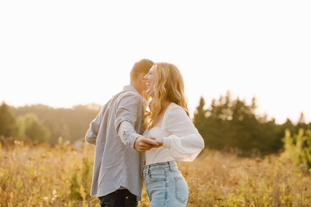 Engaged couple sharing a playful moment in a lush Bemidji field during golden hour