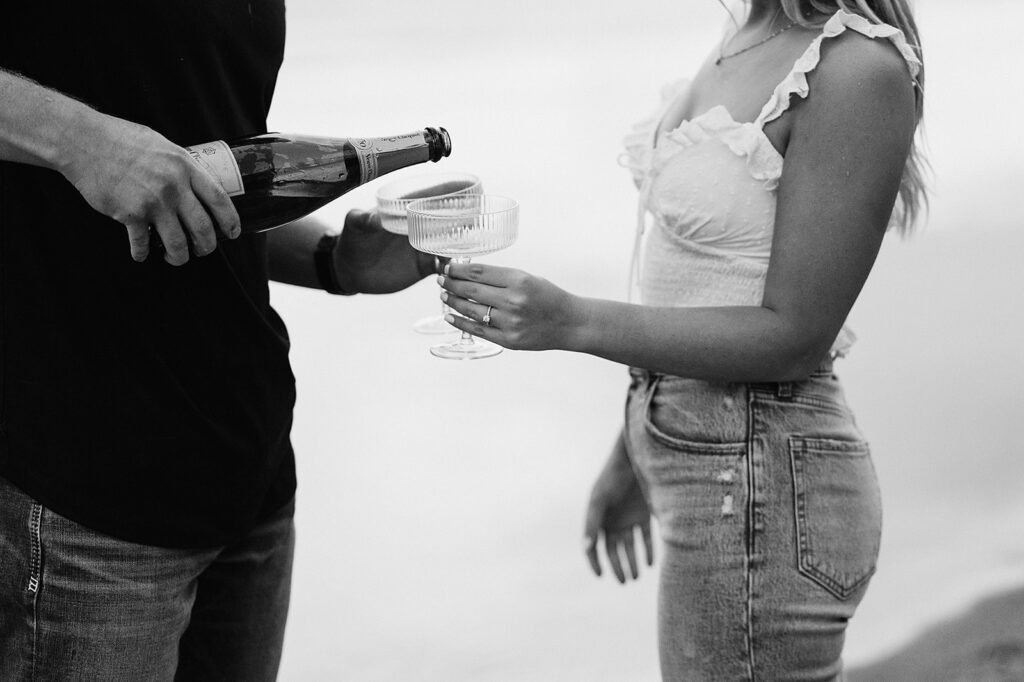 Engaged couple popping a bottle of champagne and enjoying drinks at the beach