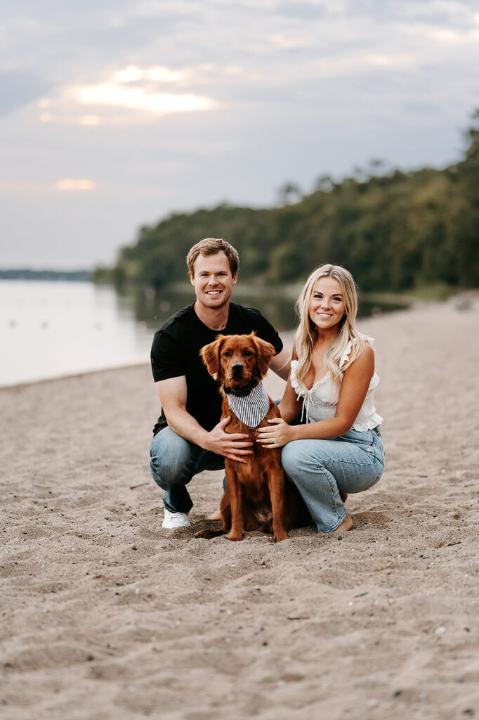 Engaged couple and their cute brown dog captured in a romantic setting by the water in Bemidji