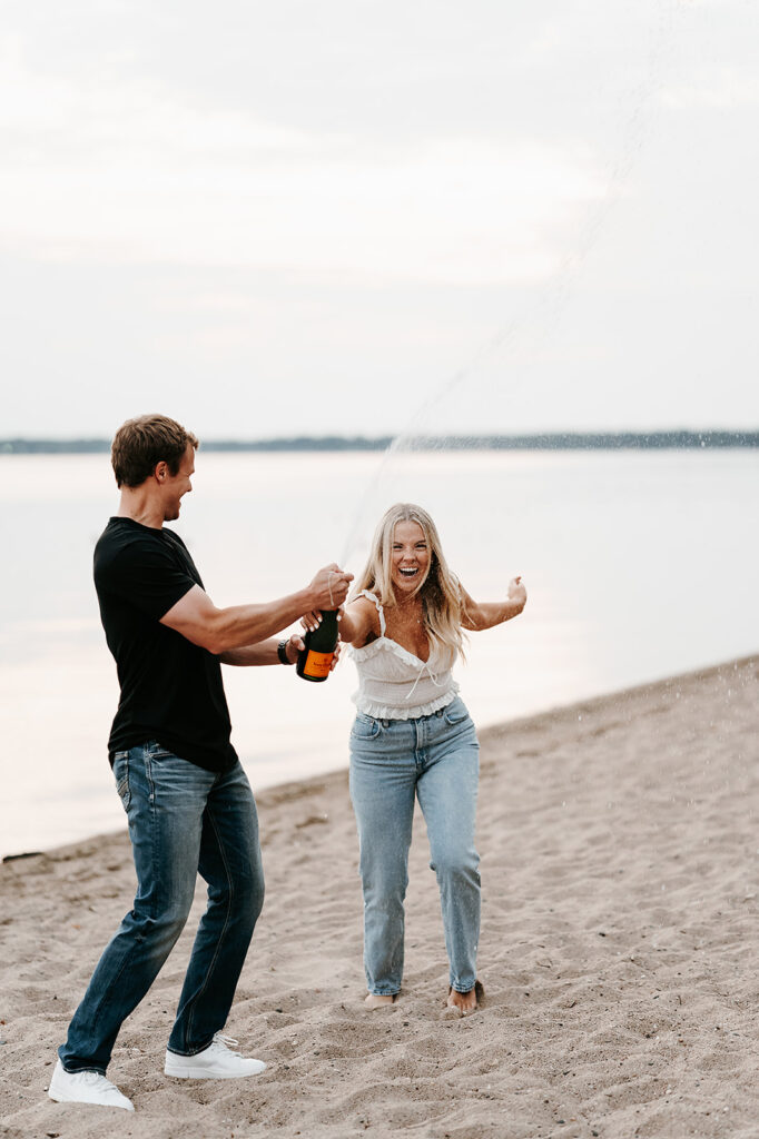 Engaged couple popping a bottle of champagne and enjoying drinks at the beach