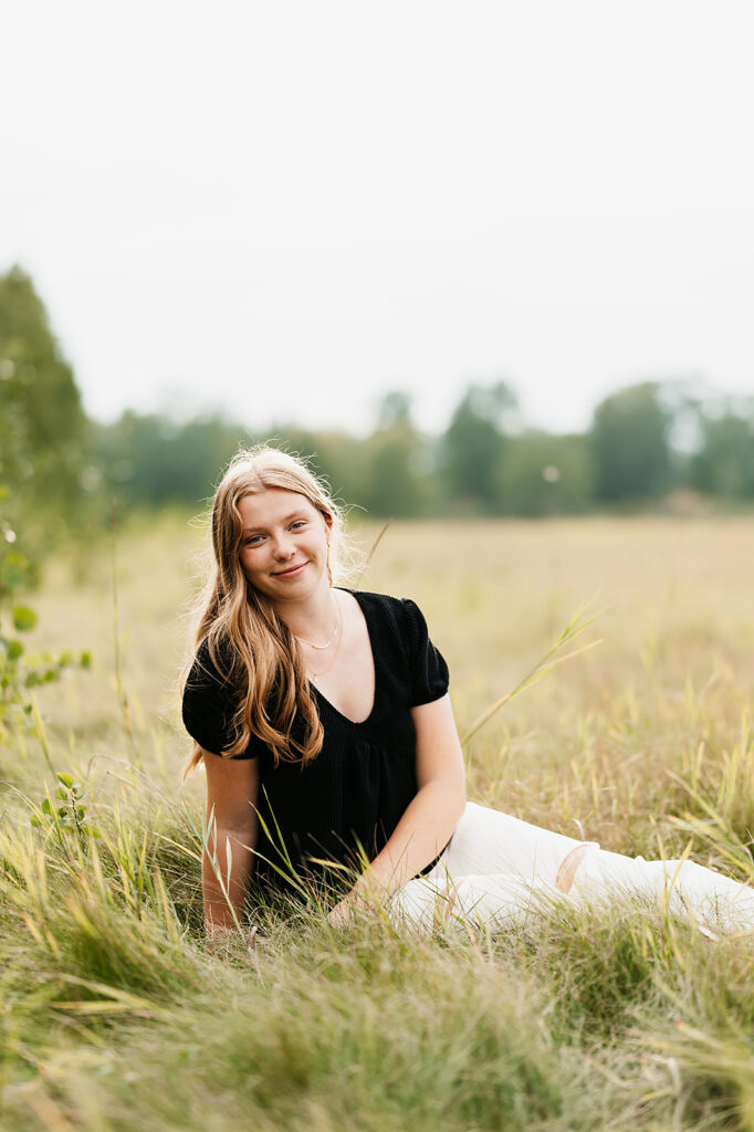A girl student smiling at Lake Bemidji State Park, surrounded by lush greenery, exemplifying the natural beauty of Minnesota in her senior photo