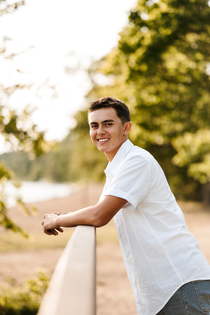 A boy student smiling at Lake Bemidji State Park, surrounded by lush greenery, exemplifying the natural beauty of Minnesota in his senior photo