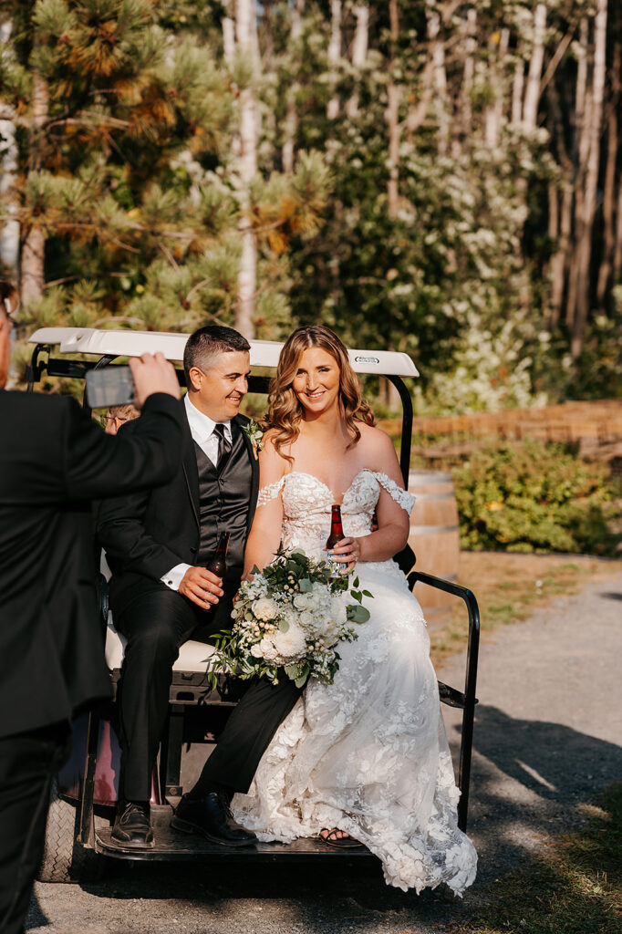 bride and groom at the back of a golf cart enjoying a beer
