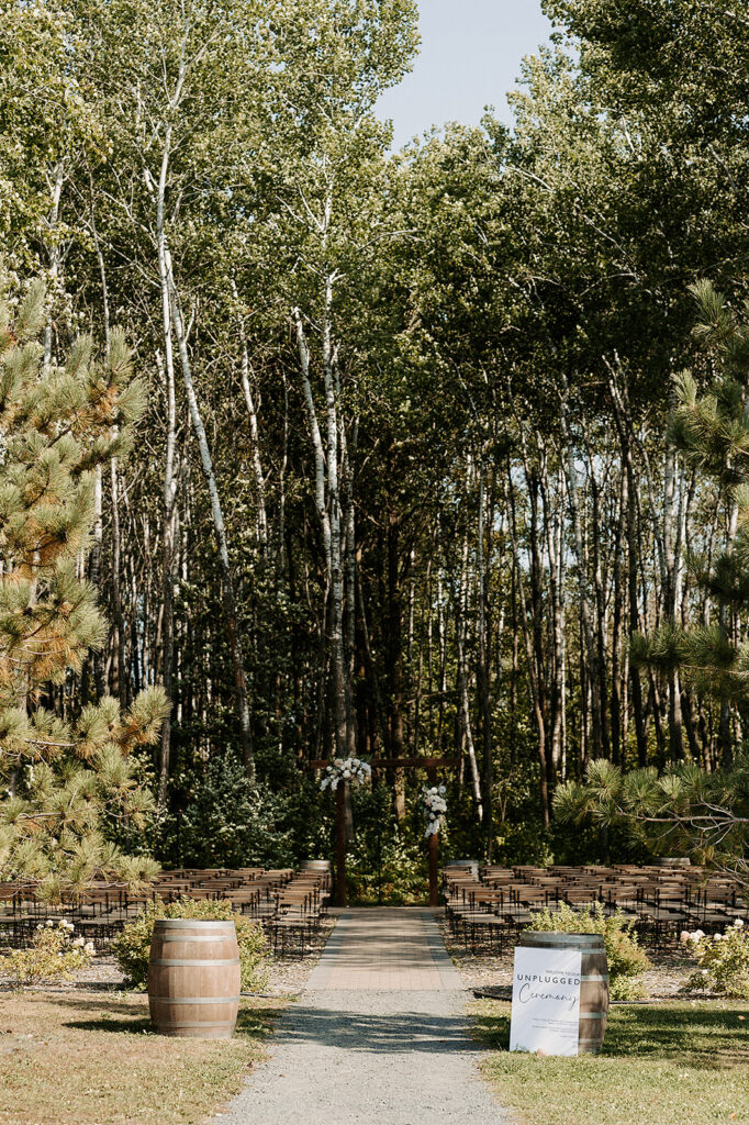 outdoor ceremony space at a bemidji wedding venue, with a forest in the backdrop and wooden chairs set up facing the arch