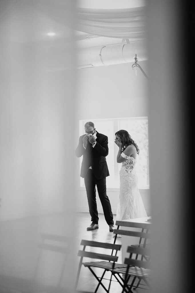 Long distance, black and white photos capturing bride and dad's first look reactions through a window, seeing their happy tears and so much love