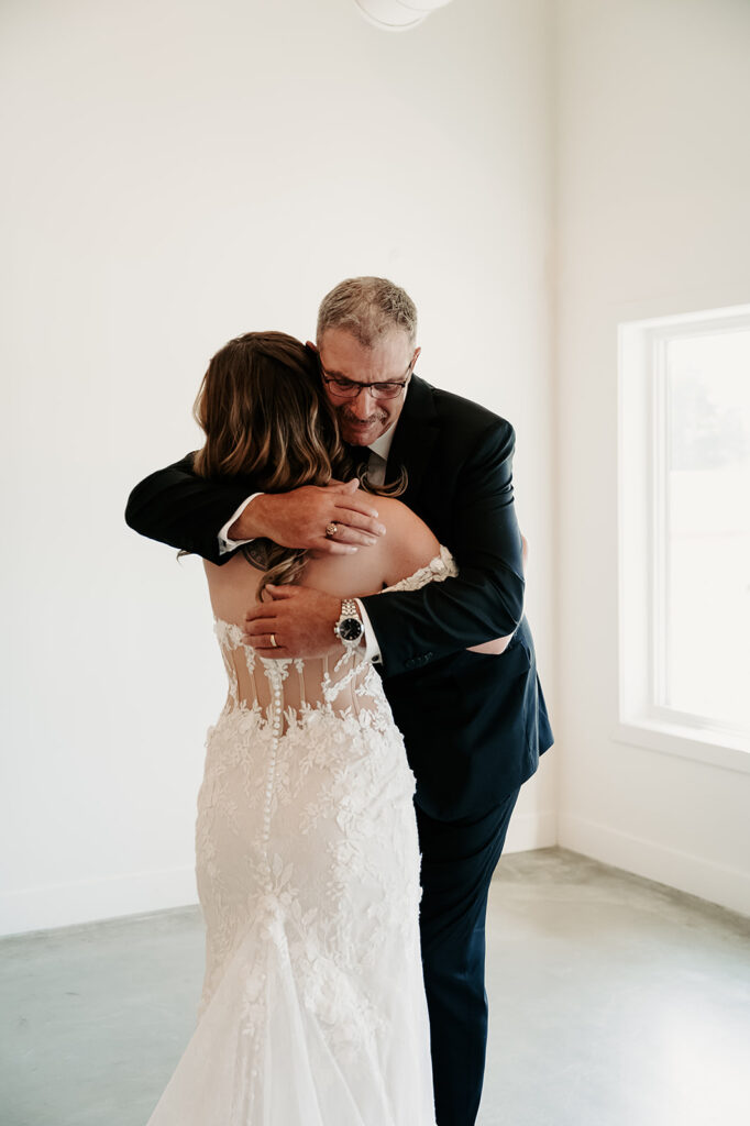 Emotional moment captured between the bride and her father during their first look at the Bluebelle Event Venue, with the bride in a stunning white gown and her father showing a tearful smile of joy.