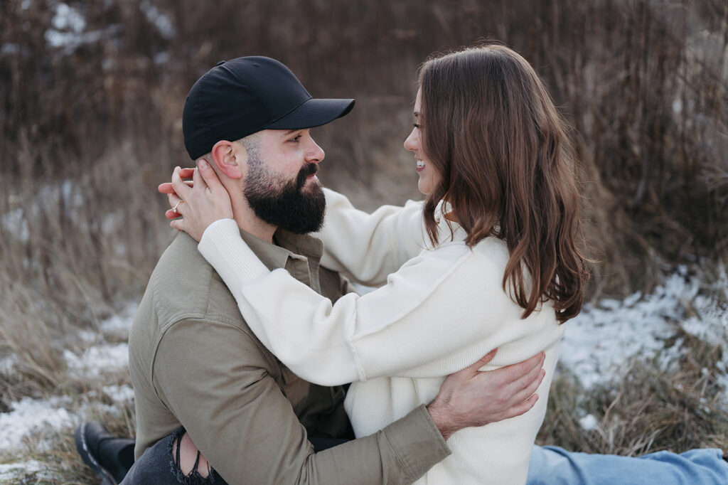 couple sitting down in a snowy field for their playful and sweet winter engagement session