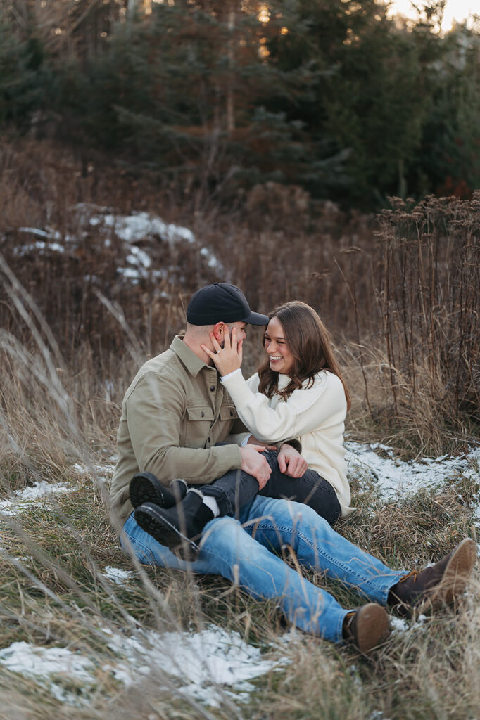 couple sitting down in a snowy field for their playful and sweet winter engagement session