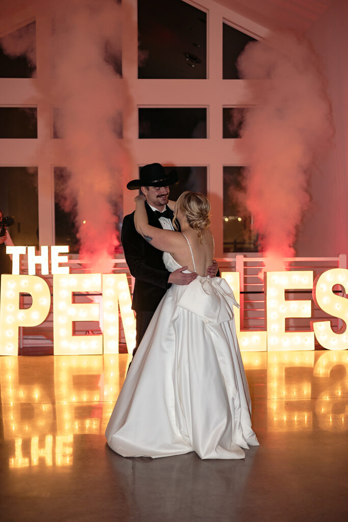 bride and groom first dance in front of their bright marquee letters spelling “The Pemble’s”