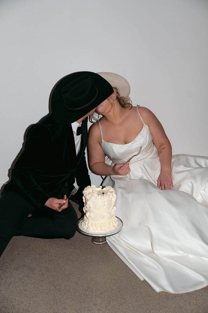 Bride and groom sitting on the floor eating cake together late at night at The Aisling