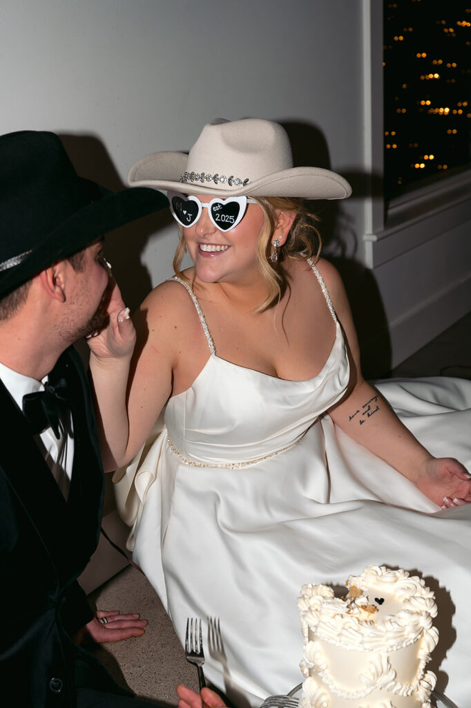 Groom laughing as bride feeds him cake during casual late-night moment at The Aisling