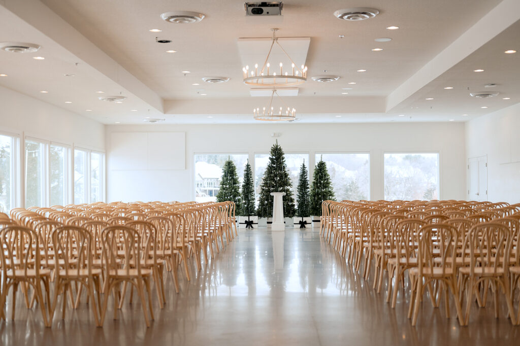 Minimalist indoor ceremony setup with evergreen trees and wooden chairs at The Aisling