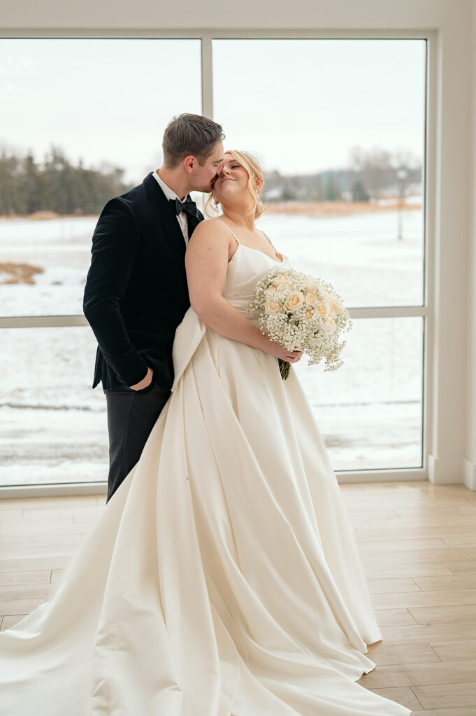 Bride and groom hugging in front of the large windows at The Aisling during winter wedding