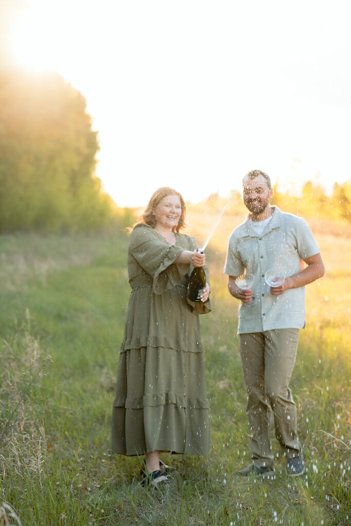 couple popping champagne in a field during golden hour