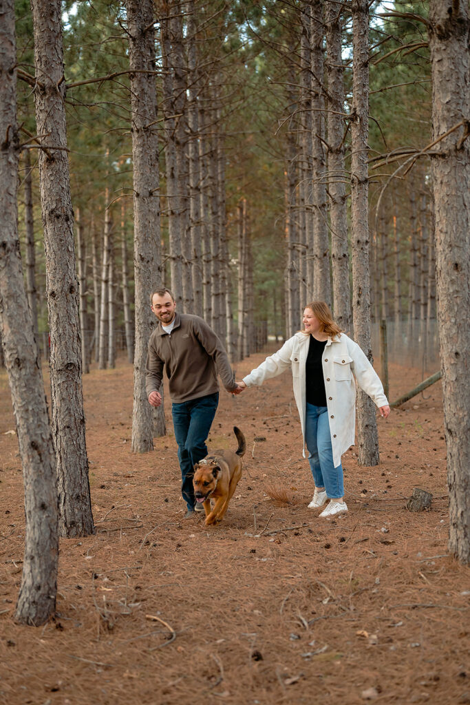 playful couple in a forest running with their dog