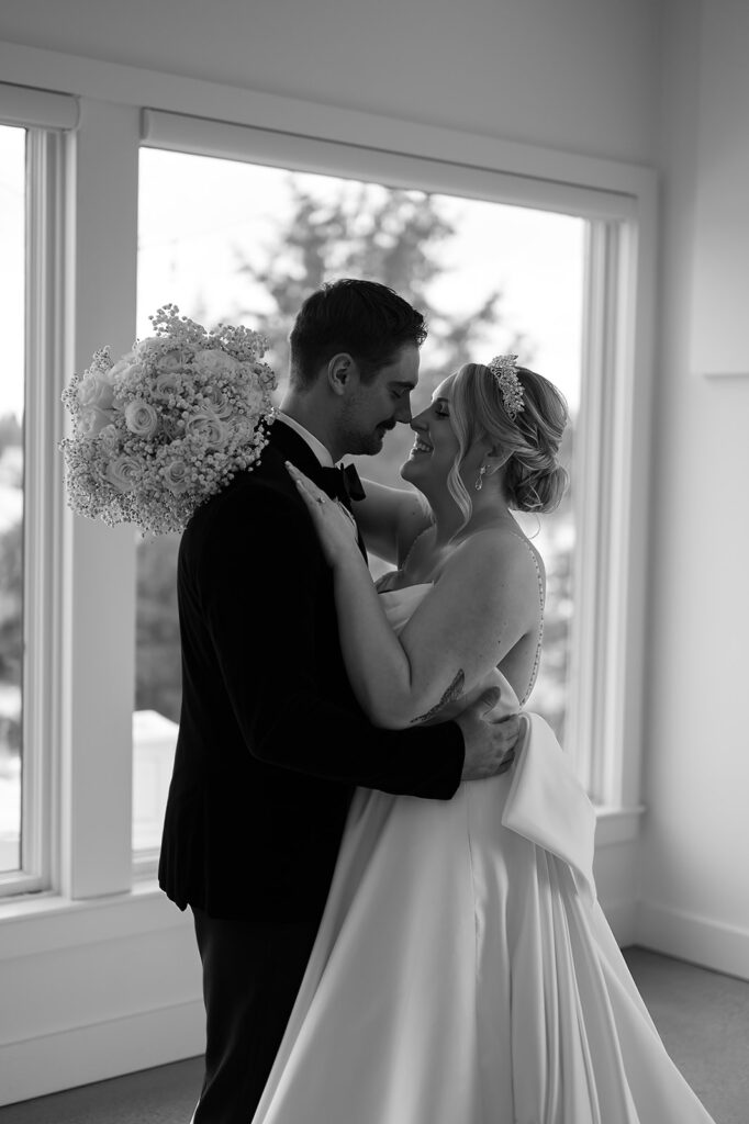 Bride and groom smiling in front of the large windows at The Aisling during winter wedding
