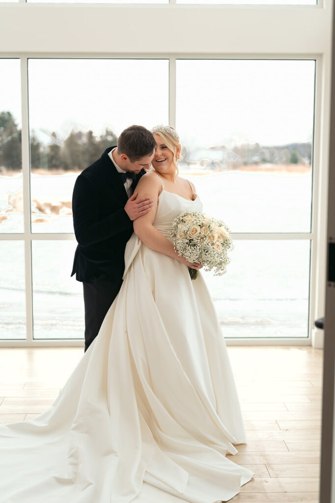 Bride and groom smiling in front of the large windows at The Aisling during winter wedding
