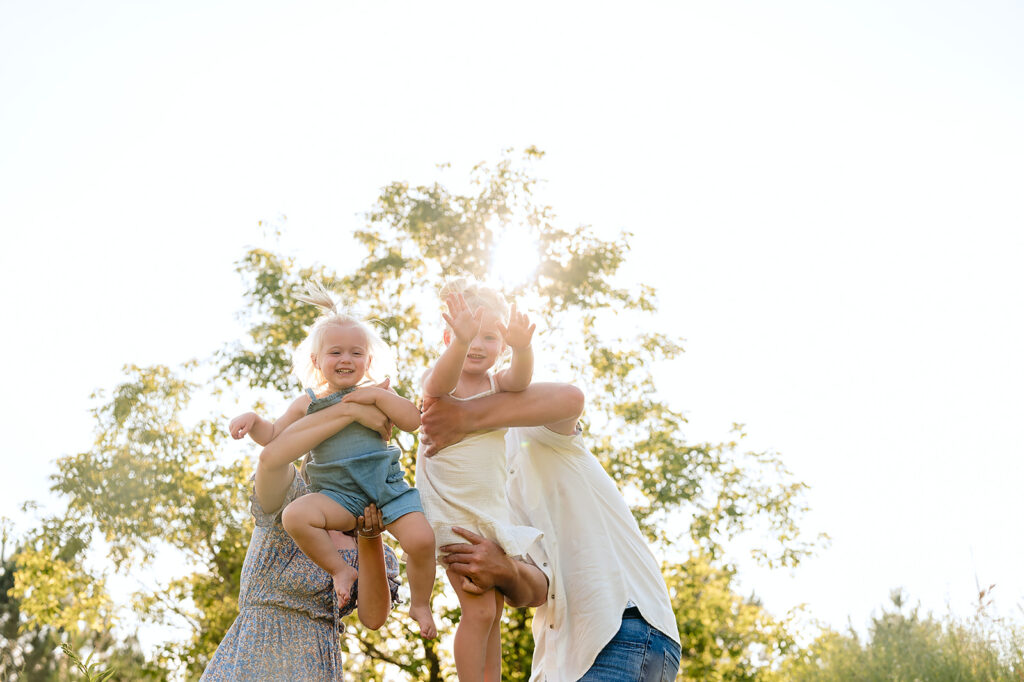 mom, dad and their two little daughters in a lush green field in Minnesota