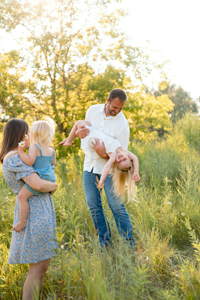 mom, dad and their two little daughters in a lush green field in Minnesota