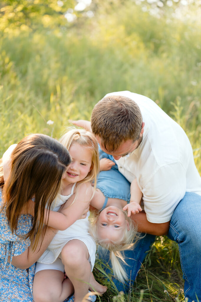 mom, dad and their two little daughters in a lush green field in Minnesota
