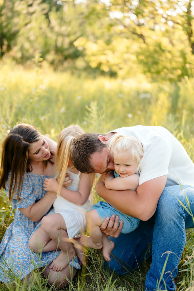 mom, dad and their two little daughters in a lush green field in Minnesota