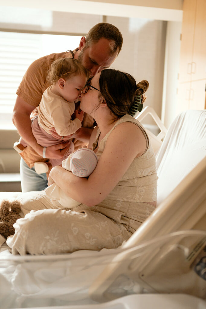 mom holding a newborn in the hospital as they introduce toddler to the baby