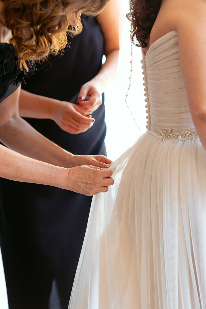 mom helping bride get into the wedding dress