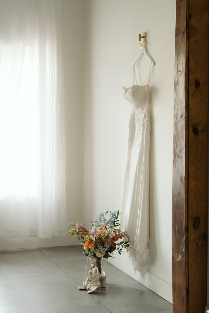 wedding details with wedding dress hanging off the wall with flowers and shoes