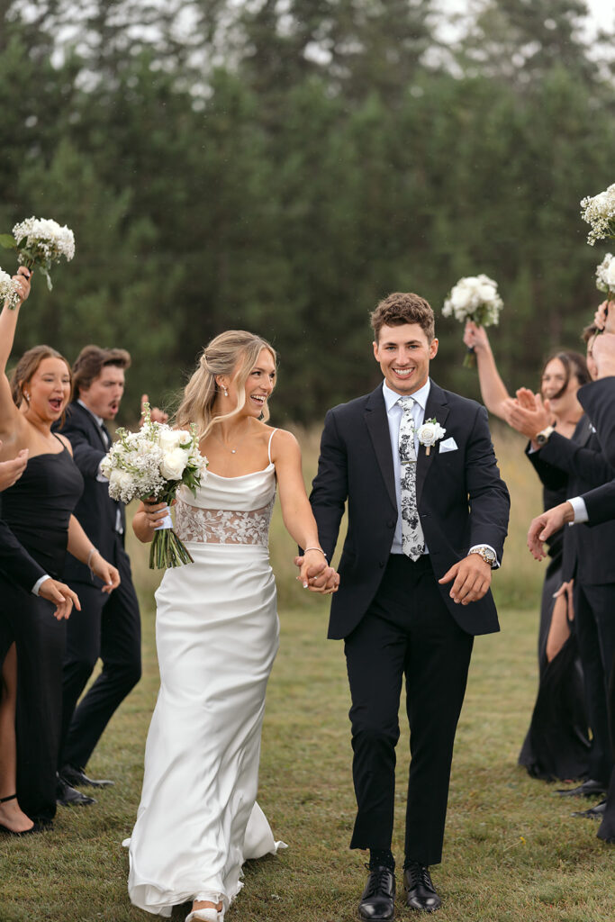 bride and groom walking while wedding party are cheering next to them