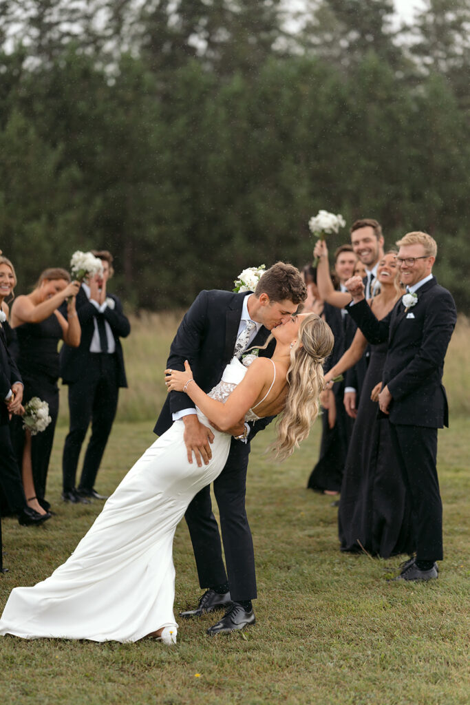 bride and groom kissing while wedding party are cheering