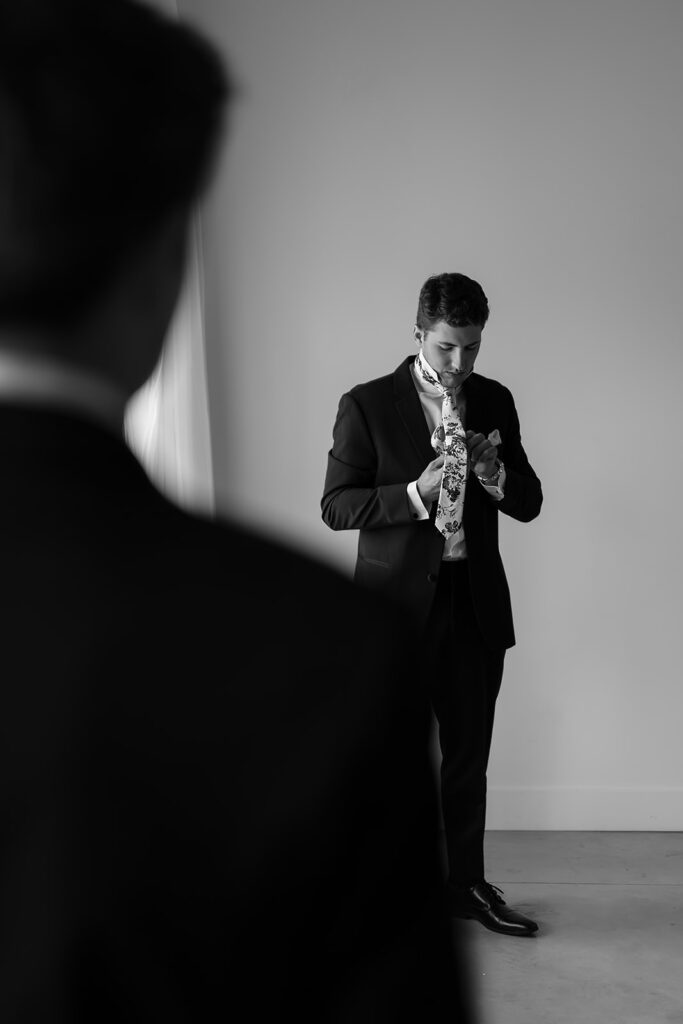 groom getting ready next to a large window inside the bluebelle event venue