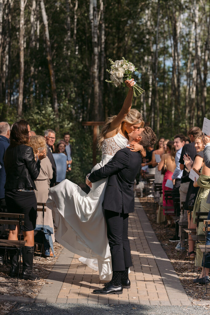 happy bride and groom kiss at the end of the aisle during the outdoor wedding ceremony at the bluebelle event venue
