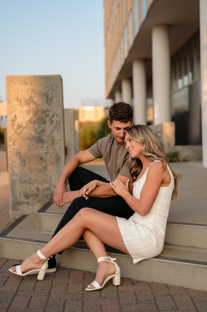 sweet couple sitting on some steps during golden hour for their downtown engagement photos in Bemidji