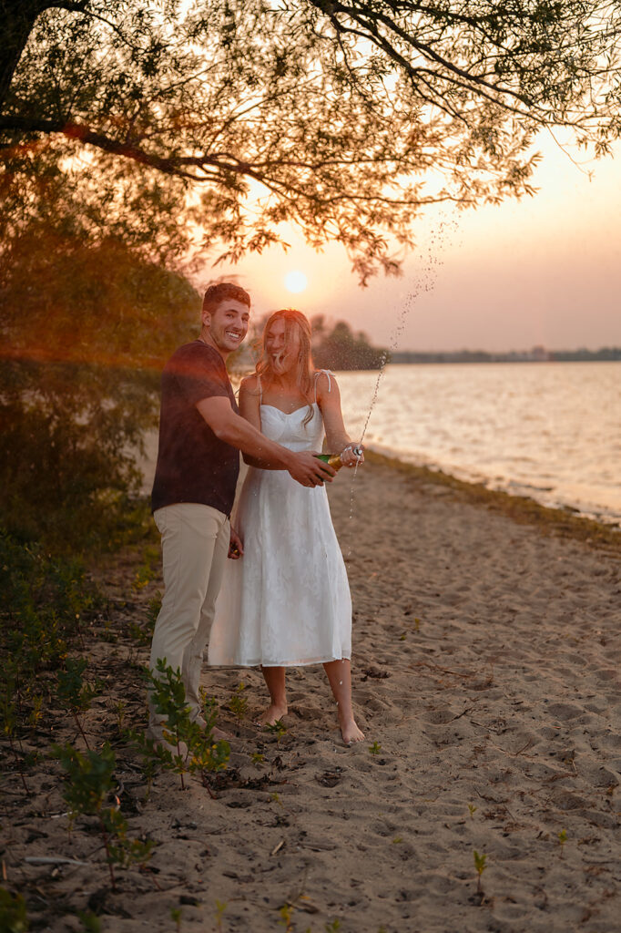 couple being popping champagne during sunset on Lake Bemidji shore