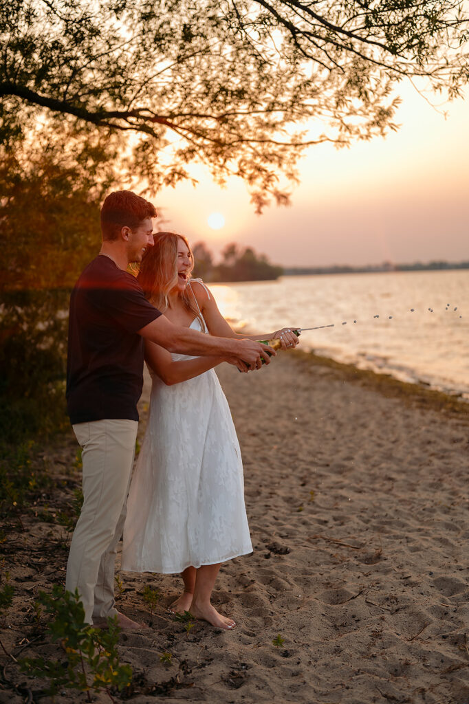 couple being popping champagne during sunset on Lake Bemidji shore