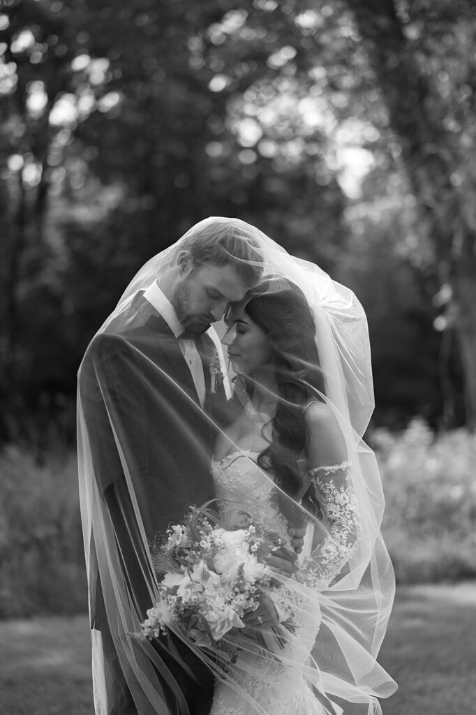 bride and groom under veil surrounded by lush green landscapes during their lakeside wedding in bemidji mn