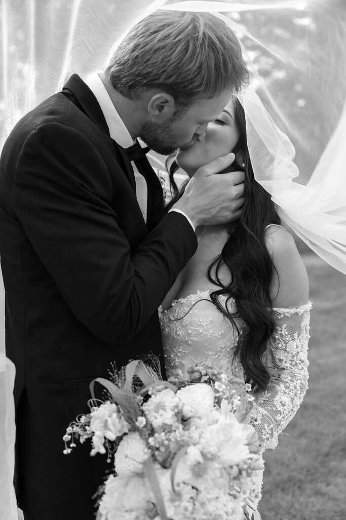 bride and groom under veil surrounded by lush green landscapes during their lakeside wedding in bemidji mn