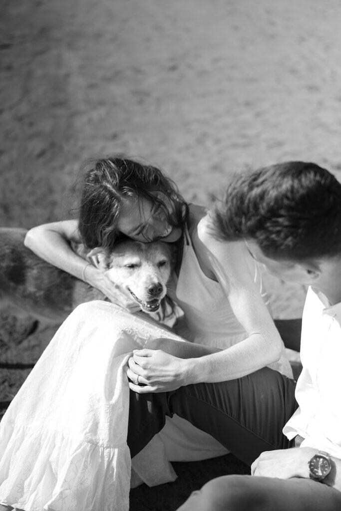 sweet couple snuggling their dog on a lake shore