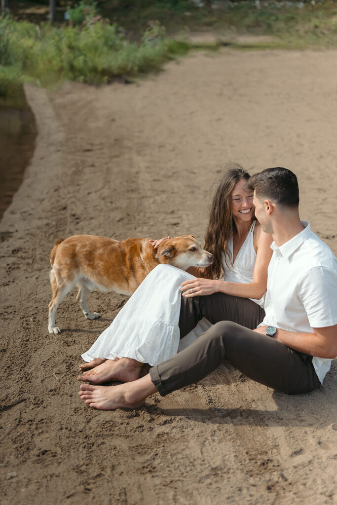 sweet couple snuggling their dog on a lake shore
