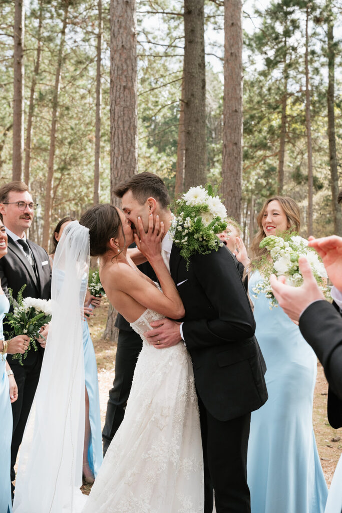bride and groom kissing while being cheered on by their wedding party