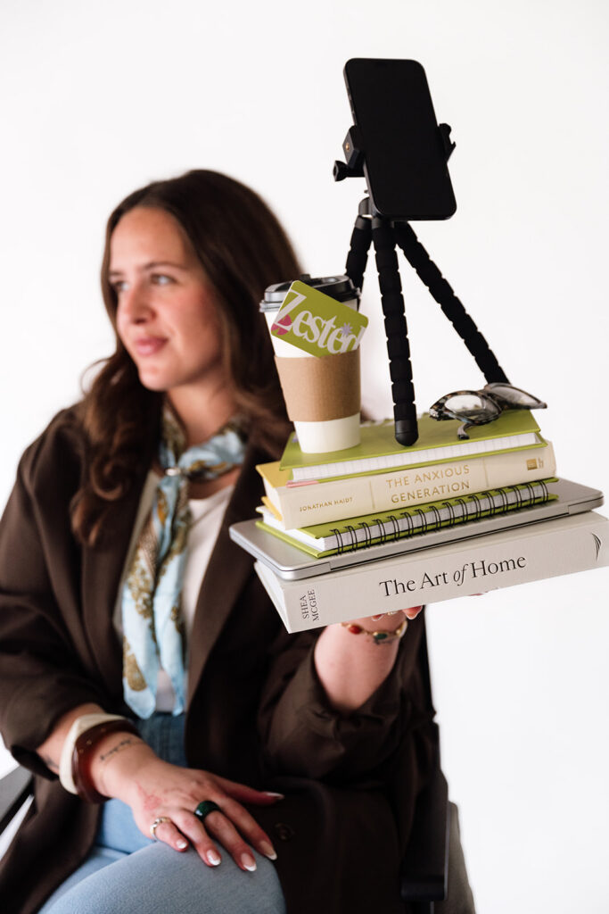 Brand photographer’s content creation setup with a phone tripod, coffee, notebooks and business books.