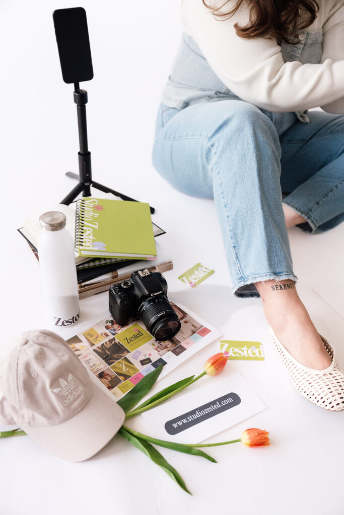 Brand photographer’s content creation setup with a phone tripod, coffee, notebooks and business books.