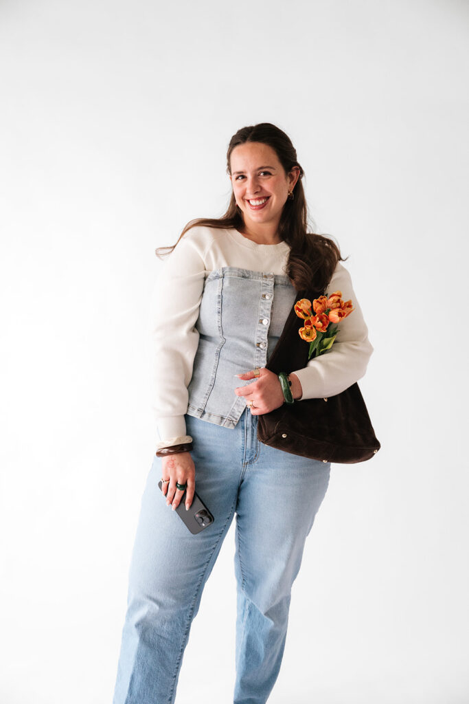 Smiling business owner holding her phone, tote bag and orange tulips during a personal branding photoshoot.