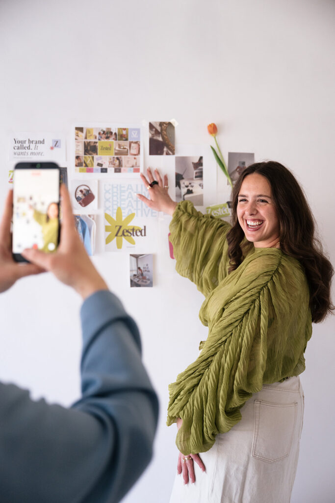 Behind-the-scenes view of a brand photographer capturing a business owner beside her colorful mood board.